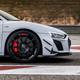 a grey 2023 audi r8 gt's front end, seen from the right hand side of the car. the car's black wheel, red brake caliper, and black 'v10' badge are all visible.
